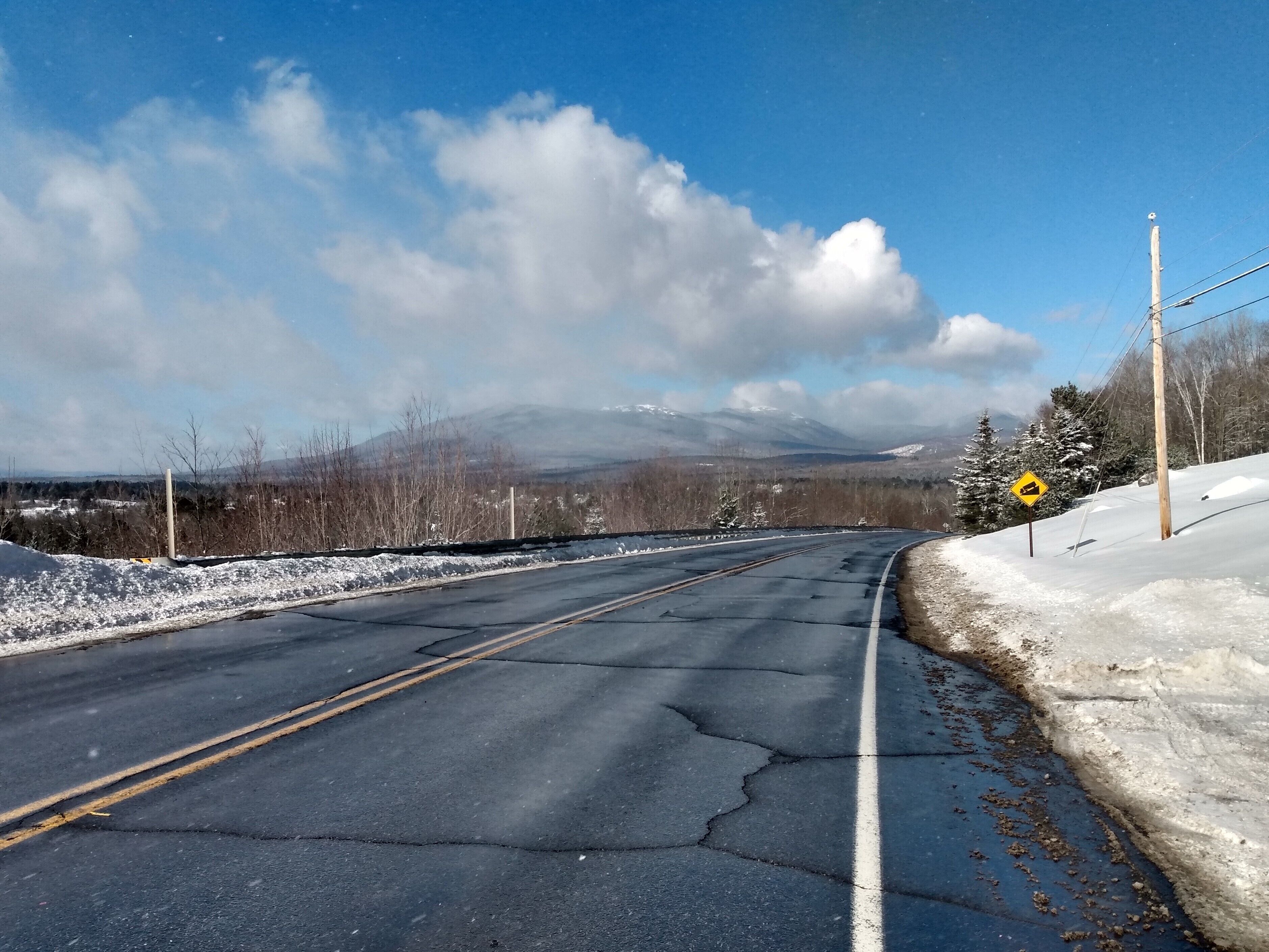 A snow-covered road with a mountain in the background and a clear sky.