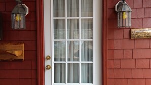 A white door with a glass panel, flanked by two lantern-style lights, set in a red brick wall. - Rural Maine cabin near Flagstaff Lake and Sugarloaf (Highland Plantation)