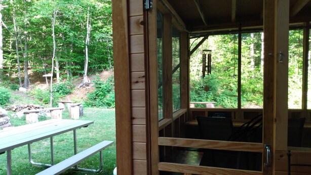 A wooden cabin with a dining area and a window overlooking a forest. - Rural Maine cabin near Flagstaff Lake and Sugarloaf (Highland Plantation)