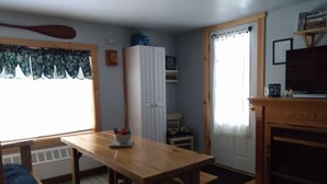 A cozy living room with a wooden table, a white cabinet, a fireplace, and a television on a stand. - Rural Maine cabin near Flagstaff Lake and Sugarloaf (Highland Plantation)