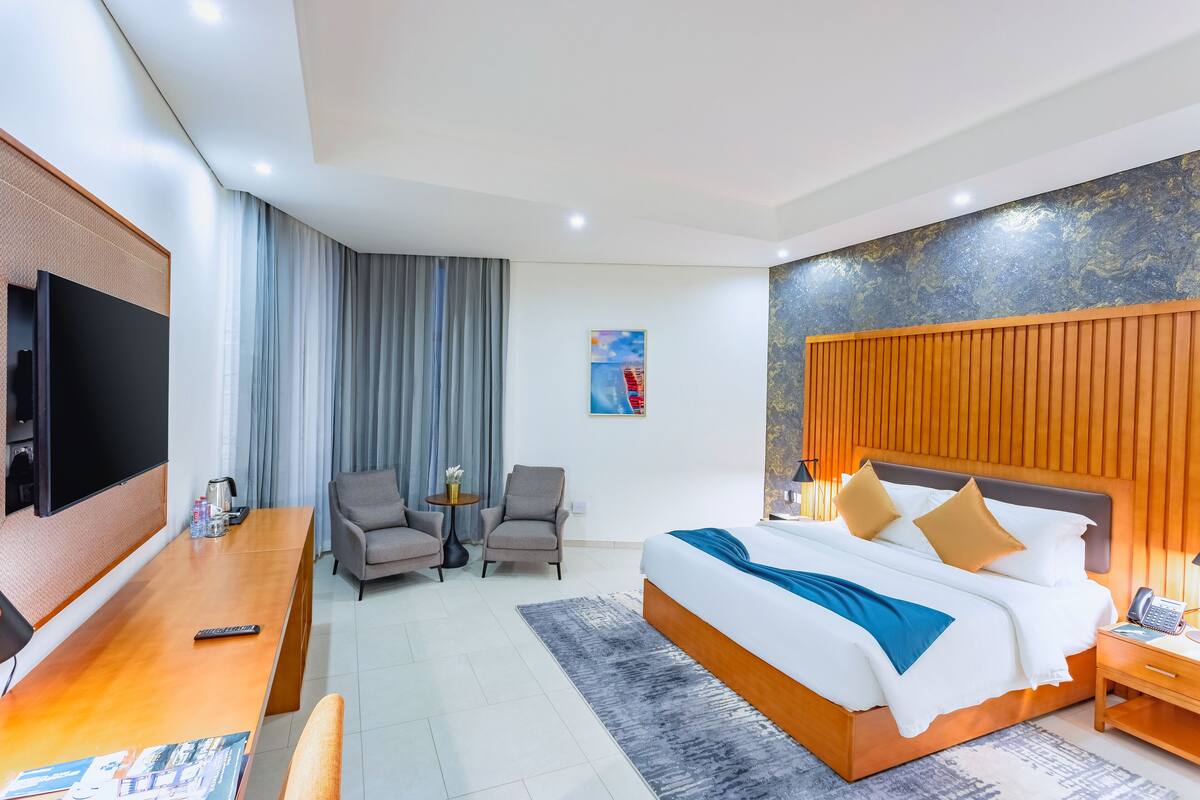 Ein modernes Hotelzimmer mit einem großen Bett, einem Schreibtisch, einem Fernseher und einer Sitzecke mit zwei Stühlen.