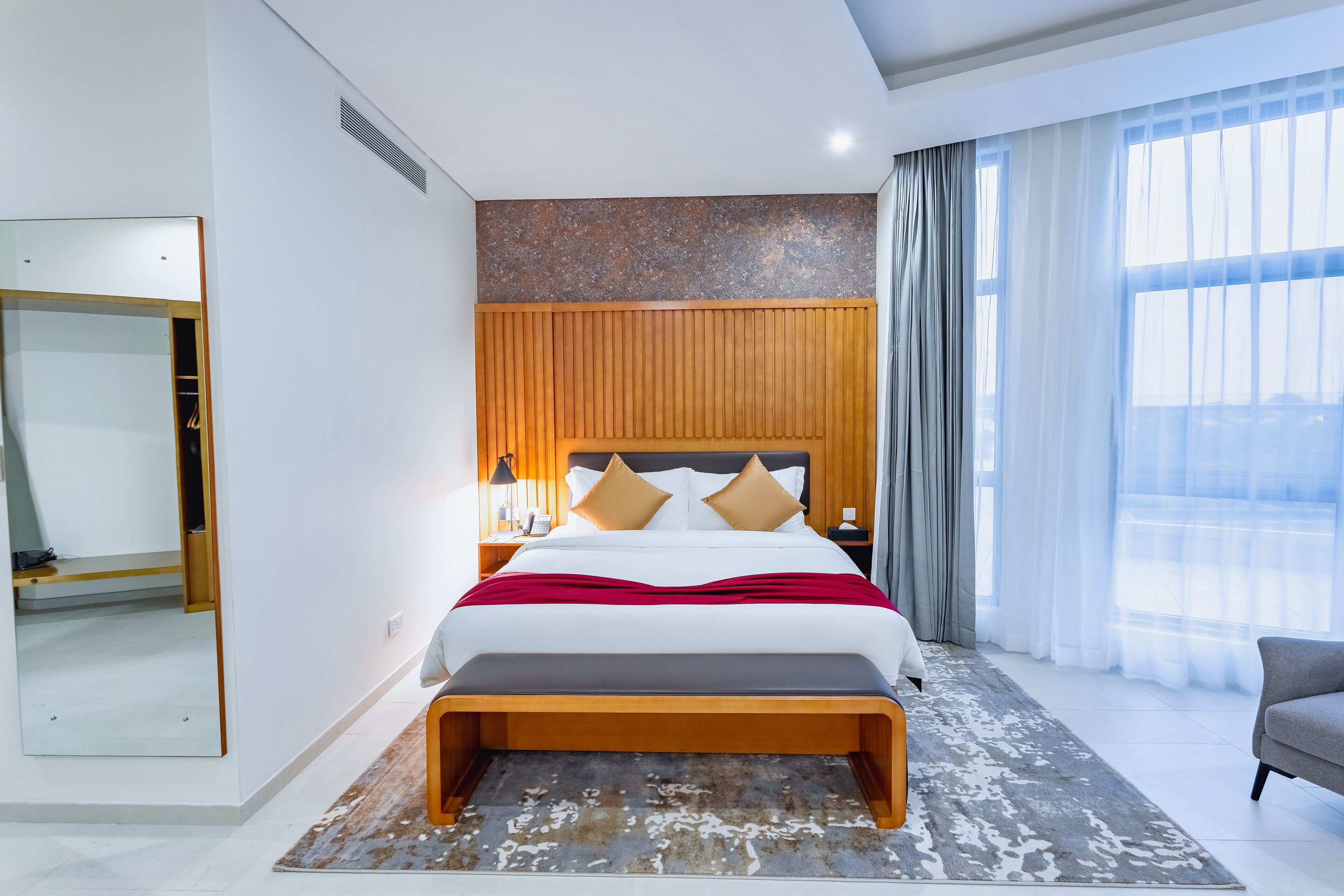 Habitación de hotel moderna con una cama grande, cabecera de madera y vistas a la ciudad a través de amplios ventanales.