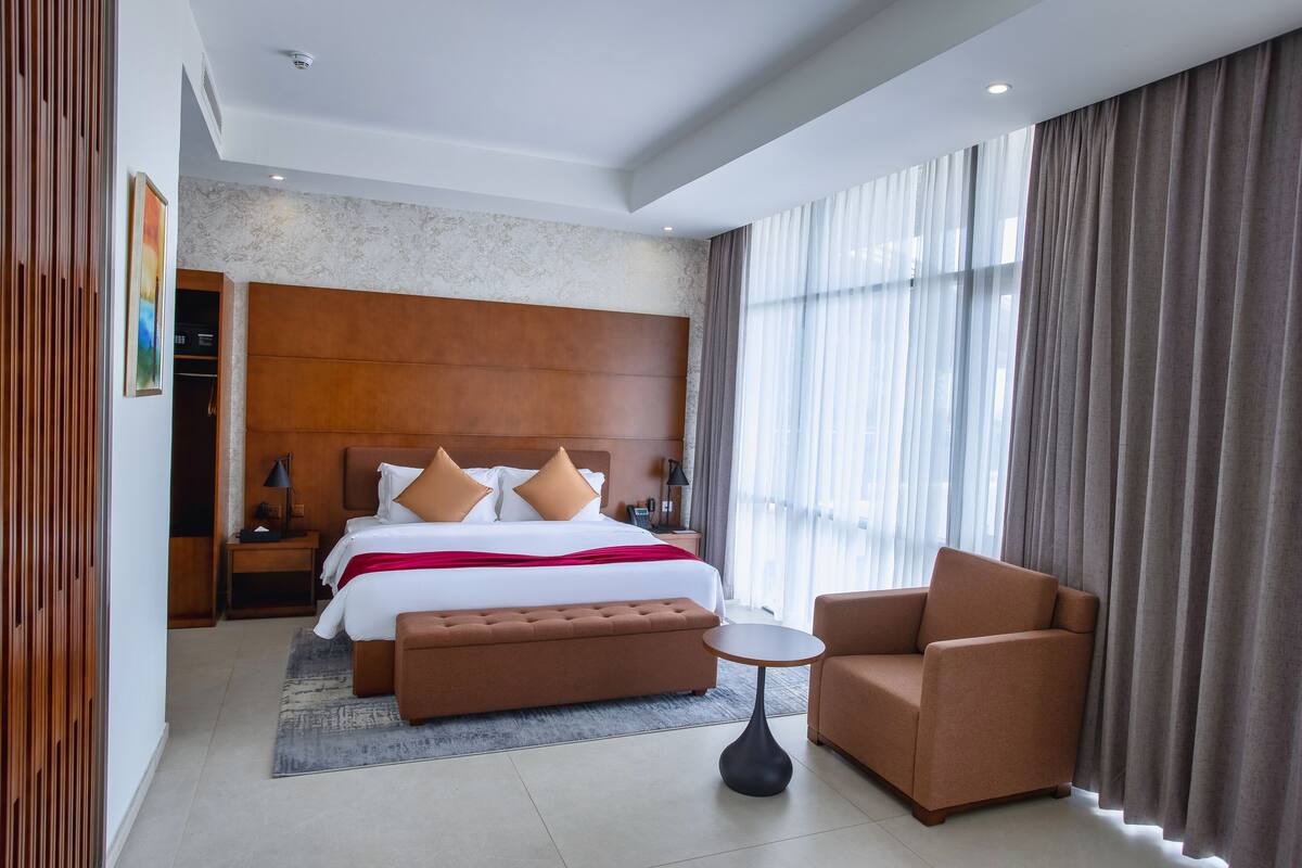 Ein modernes Hotelzimmer mit einem großen Bett, einem Holzkopfteil, einem kleinen runden Tisch und einer Couch.