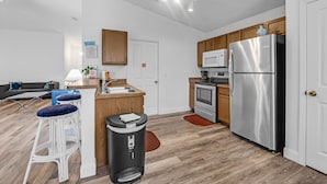 A modern kitchen with wooden cabinets, stainless steel appliances, a bar stool area, and a trash bin. - Sunshine & Splash + Disney area pool home (Davenport)