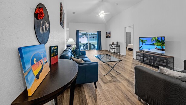 A modern living room with a sofa, coffee table, and TV. There is a painting on the wall and a welcome sign. - Sunshine & Splash + Disney area pool home (Davenport)