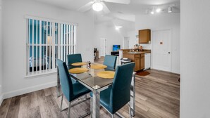 A modern dining area with a glass table, teal chairs, and a ceiling fan. - Sunshine & Splash + Disney area pool home (Davenport)