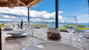 Una mesa de comedor con platos, vasos y una botella de vino, con vistas a un lago y montañas pintorescos.