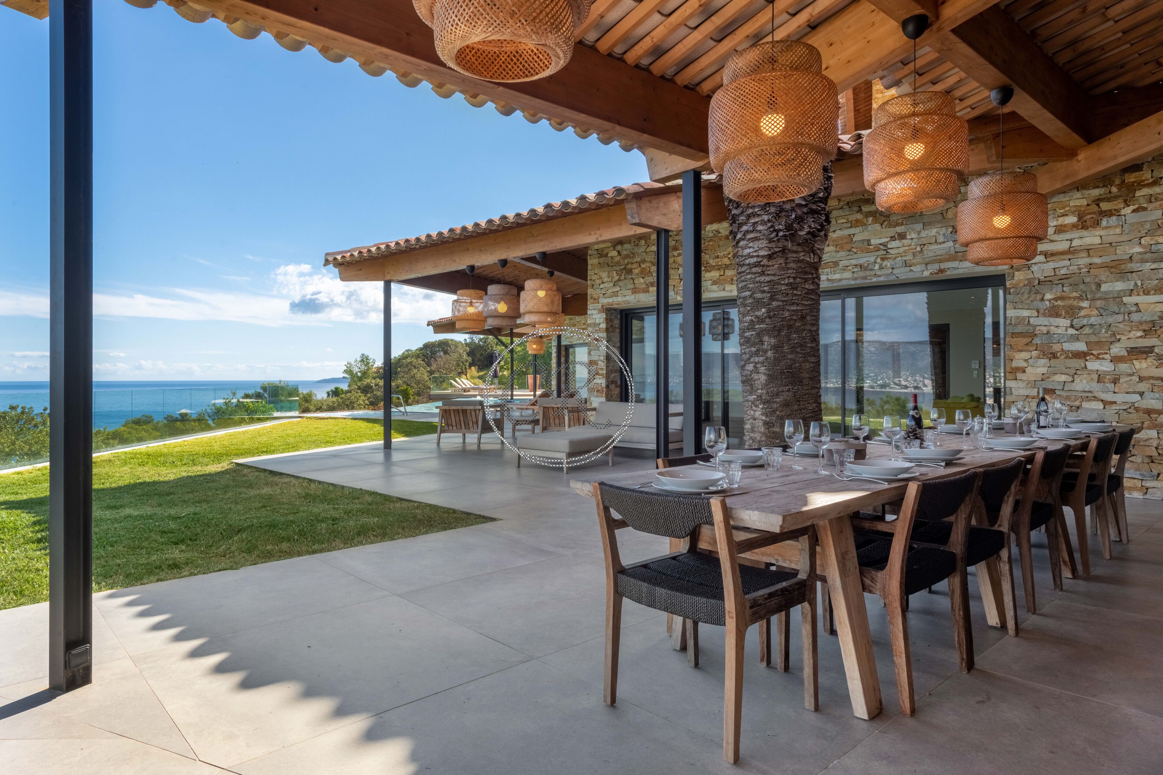 An outdoor dining area with a view of the ocean, stone walls, and woven light fixtures.