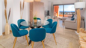 A modern living room with a glass dining table, blue chairs, and a view of the ocean through large windows. - Coto Real 2359 Lovely apartment with sea view (Manilva)