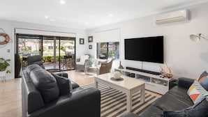 Uma sala de estar moderna com um sofá de couro preto, uma mesa de centro e uma televisão de tela plana presa à parede.
