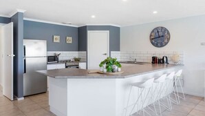 Uma cozinha moderna com uma ilha central, banquetas brancas e um relógio na parede.