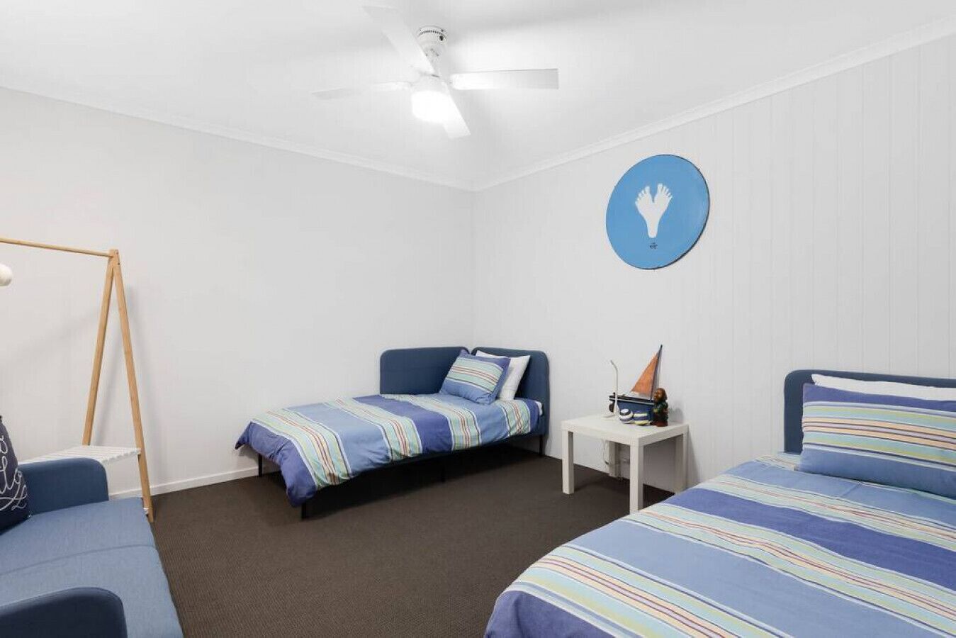Un dormitorio con dos camas individuales, una mesita pequeña, un ventilador de techo y un letrero redondo sujeto a la pared.