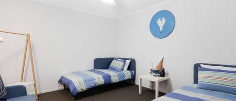 Un dormitorio con dos camas individuales, una mesita pequeña, un ventilador de techo y un letrero redondo sujeto a la pared.