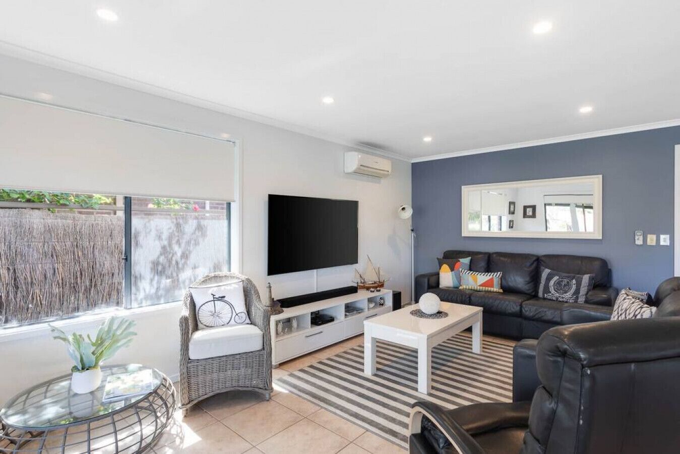 A modern living room with a flat-screen TV, a sofa, a coffee table, and a wicker chair.