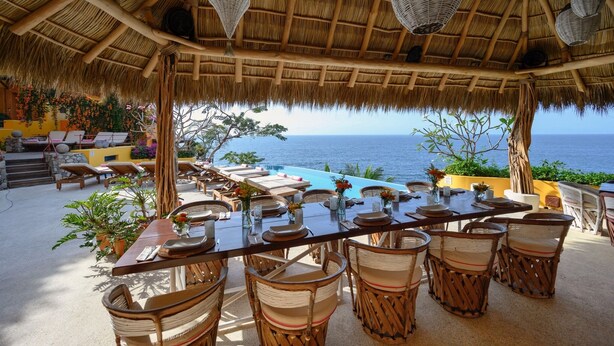 An outdoor dining area with thatched roof, wicker furniture, and a view of the ocean.