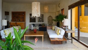A spacious living area with a white sofa set, a wooden coffee table, and a large plant.