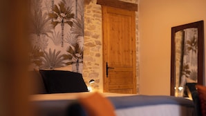 A bedroom with a bed, a wooden door, and a wall with a palm tree pattern. - 3 gîtes, swimming pool, 6 bd / 13 p - Puy du Fou / Marais poitevin / Mervent / Vouvant (Rives du Fougerais)