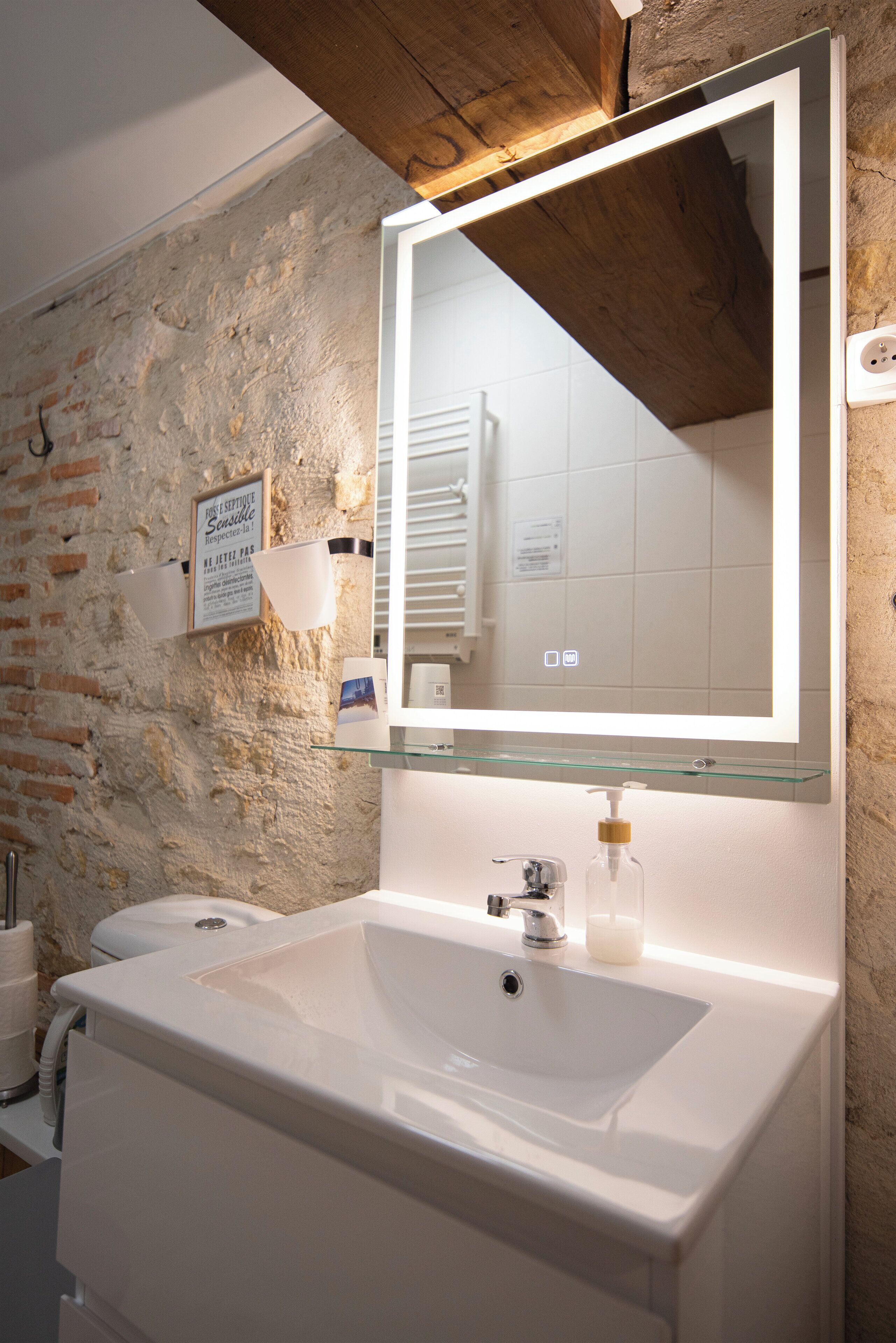 A bathroom with a large mirror, white sink, and a brick wall.