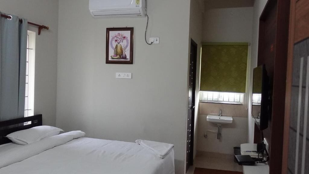 Una habitación de hotel con cama, aire acondicionado de pared, un cuadro enmarco, ventana con cortinas, lavabo y televisor.