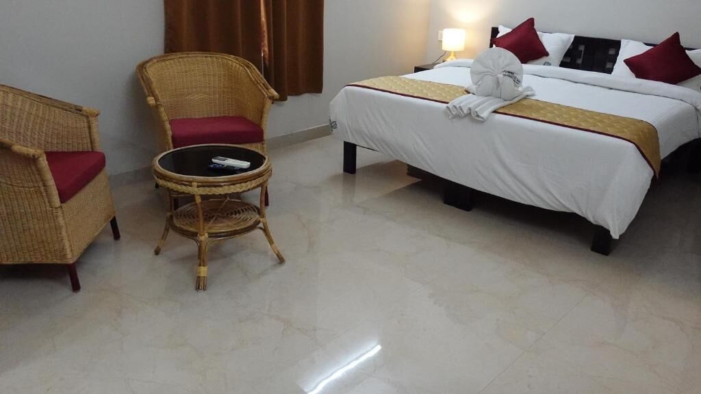 Una habitación de hotel con una cama, dos sillones de mimbre, una mesita redonda y una lámpara.