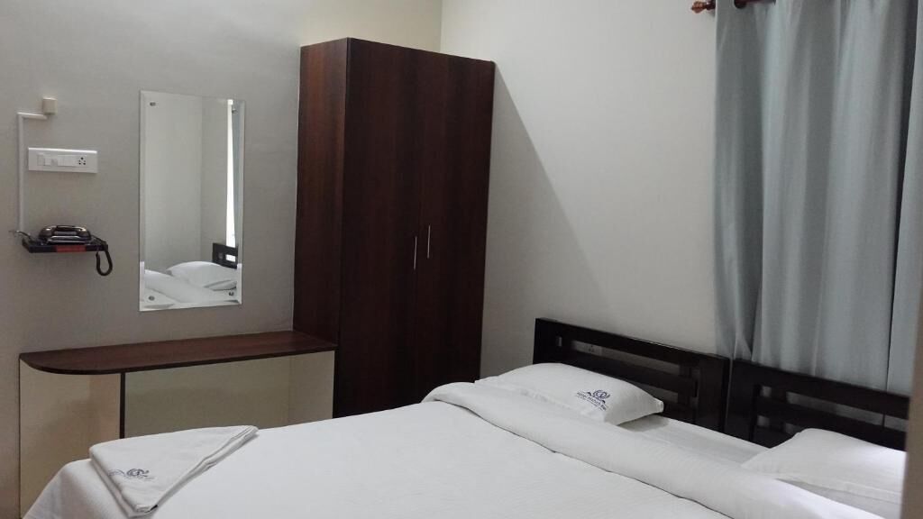 A hotel room with a bed, a wardrobe, a mirror, a telephone, and a window with curtains.