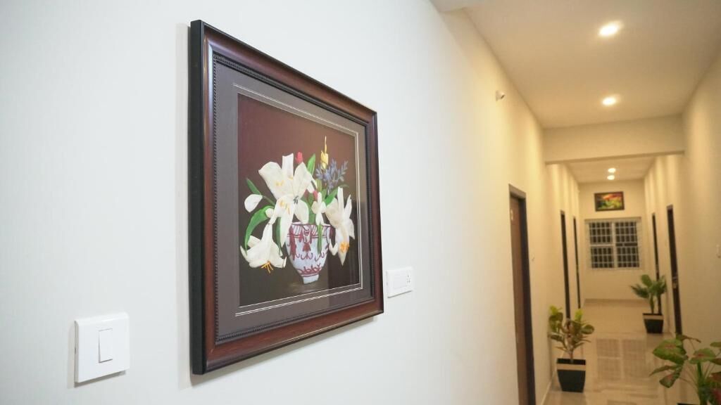 A hallway with a framed artwork on the wall, a light switch, and potted plants along the corridor.
