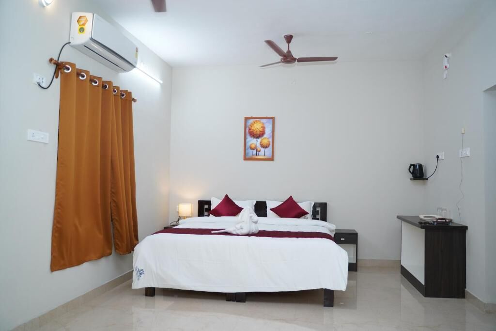 A hotel room with a bed, a desk, an air conditioner, a ceiling fan, and a painting on the wall.
