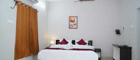 A hotel room with a bed, a desk, an air conditioner, a ceiling fan, and a painting on the wall.