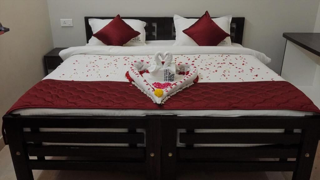 A bed with a heart-shaped decoration made of white flowers and swans, red bedding, and two red pillows.