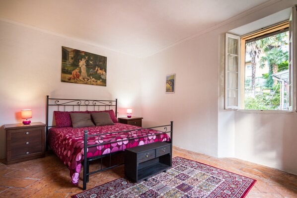 Un dormitorio con cama, mesitas de noche, un tapete y una ventana con vistas a zonas verdes.