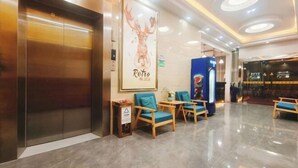 A lobby with a large elevator, teal chairs, a retro poster, and a Pepsi vending machine. - Jiangmen Danxia Hotel (Jiangmen)