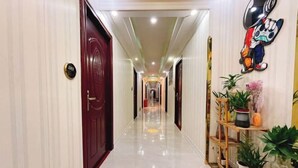 A hotel hallway with a polished floor, wooden doors, and a plant shelf on the right. - Jiangmen Danxia Hotel (Jiangmen)