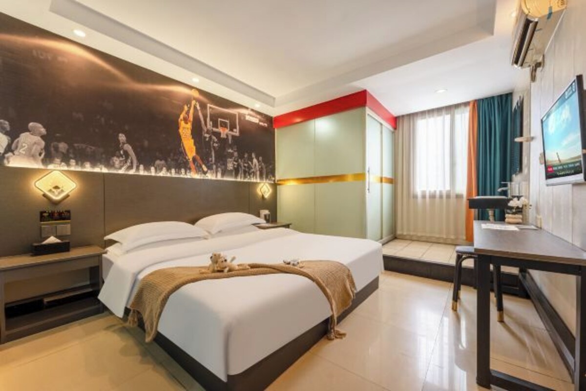 Habitació d'hotel amb llit, taula de nit, televisió penjada a la paret i escriptori amb cadira.
