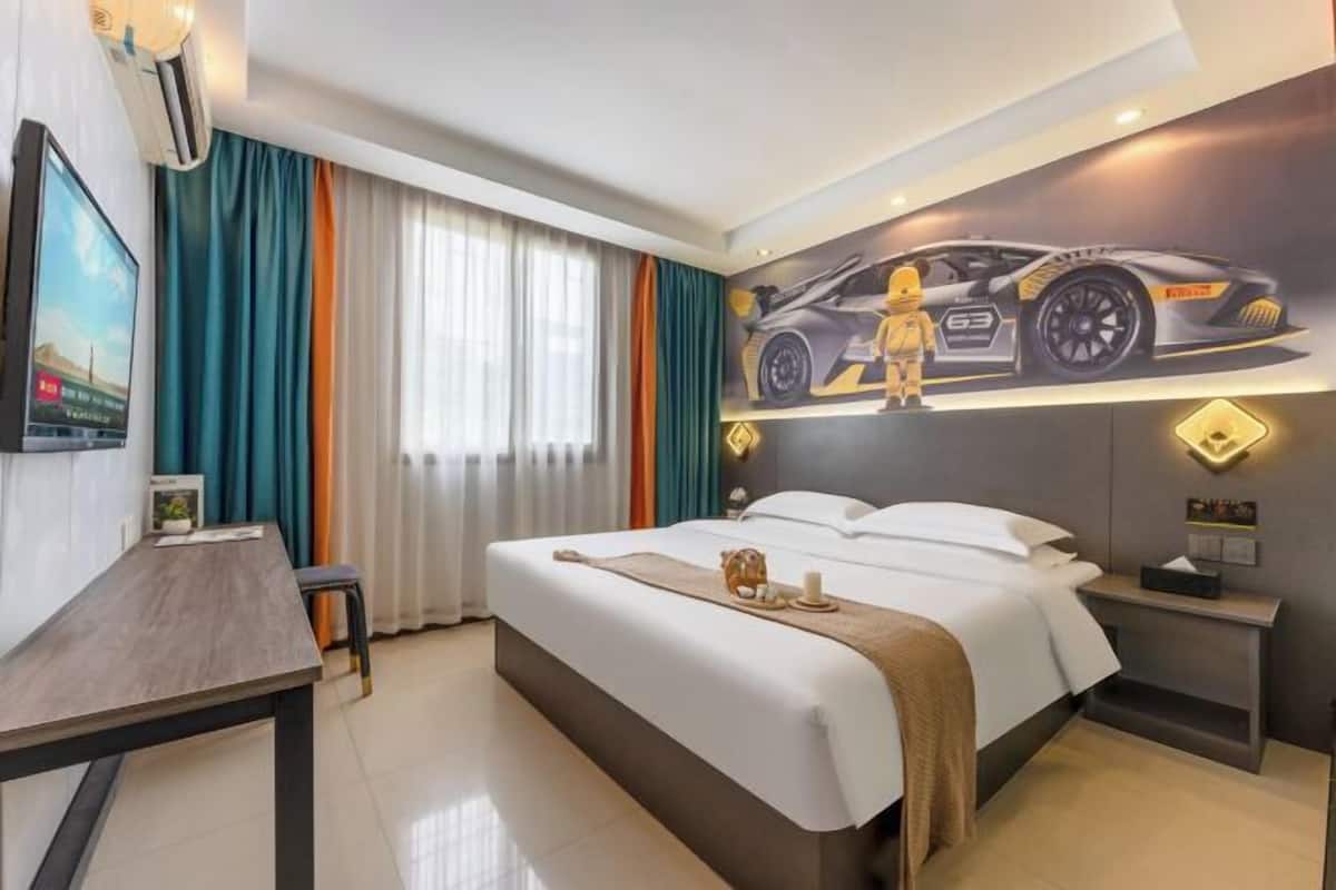 Habitación de hotel con cama, escritorio, silla, televisor, cortinas y un mural en la pared con un coche.