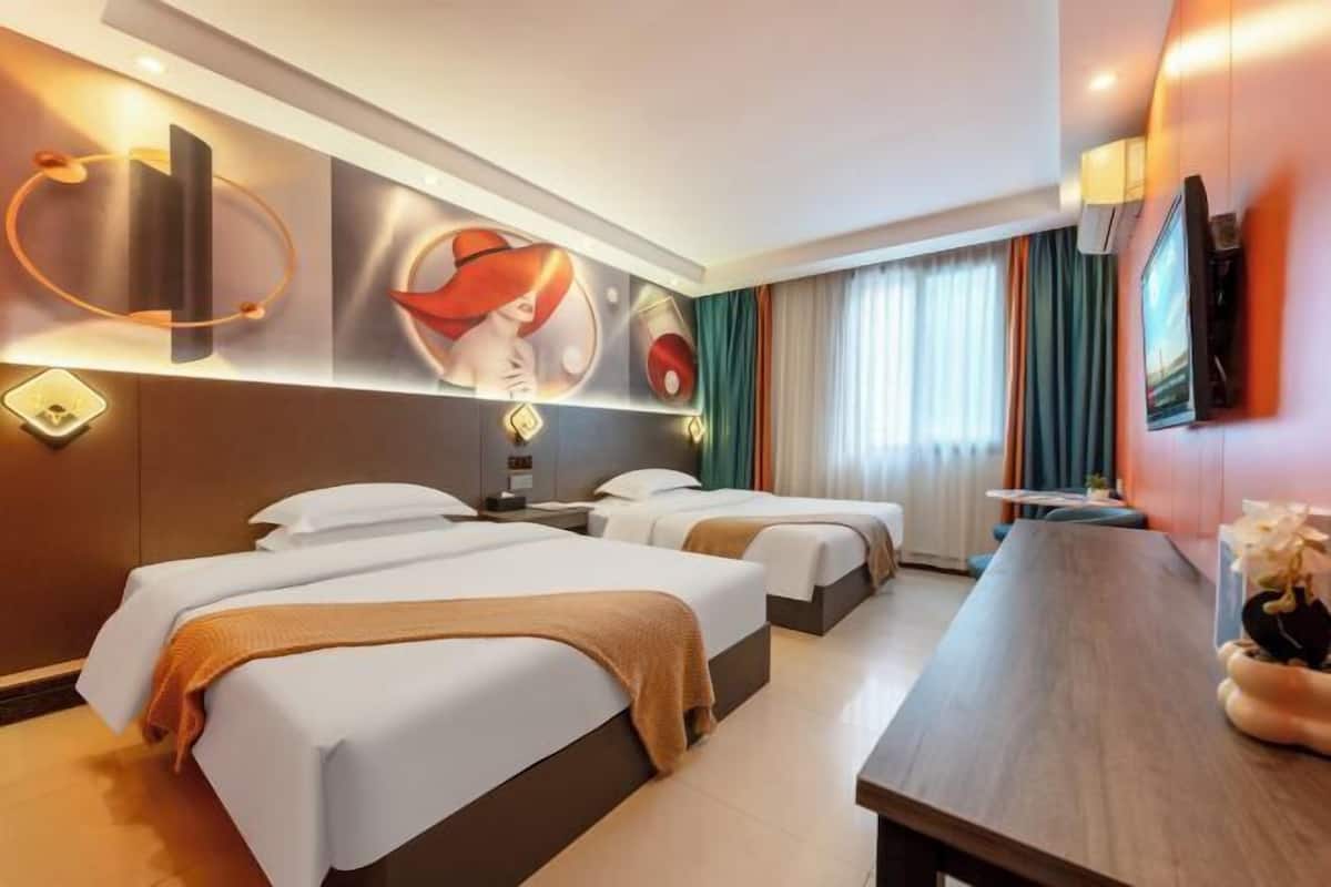 Habitación de hotel con dos camas, un escritorio de madera, un televisor y una obra de arte en la pared.
