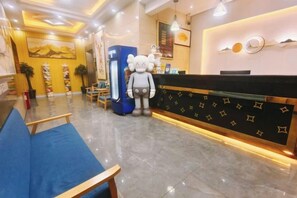 A hotel reception area with a reception desk, a blue sofa, and a large mascot statue. - Jiangmen Danxia Hotel (Jiangmen)