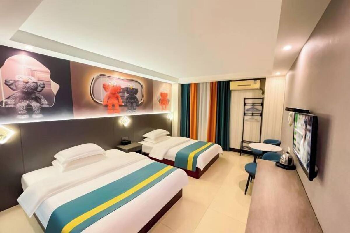 Habitación de hotel con dos camas, un escritorio, una silla, un televisor y una pared con obras de arte.