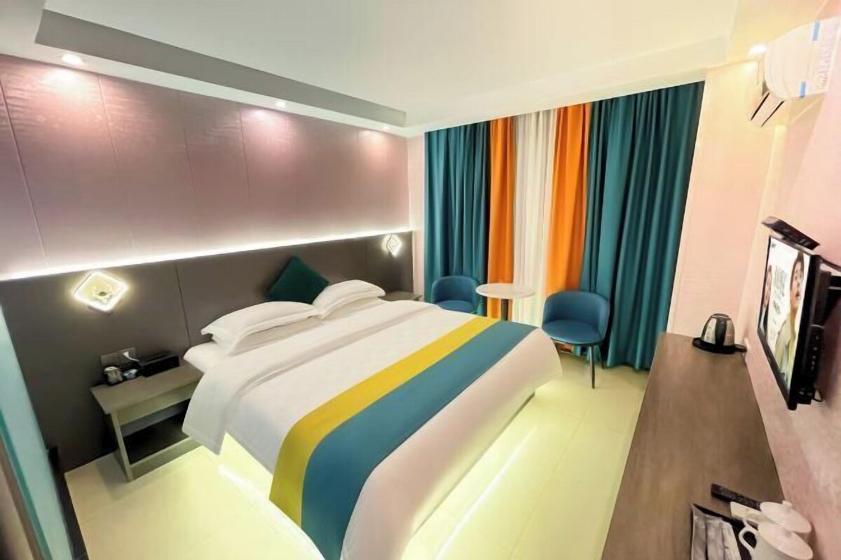 A hotel room with a bed, bedside table, chair, and a TV.