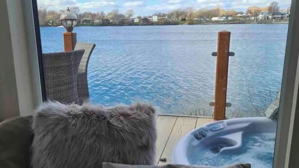 Une chambre avec vue sur un lac, un jacuzzi et un fauteuil en osier.