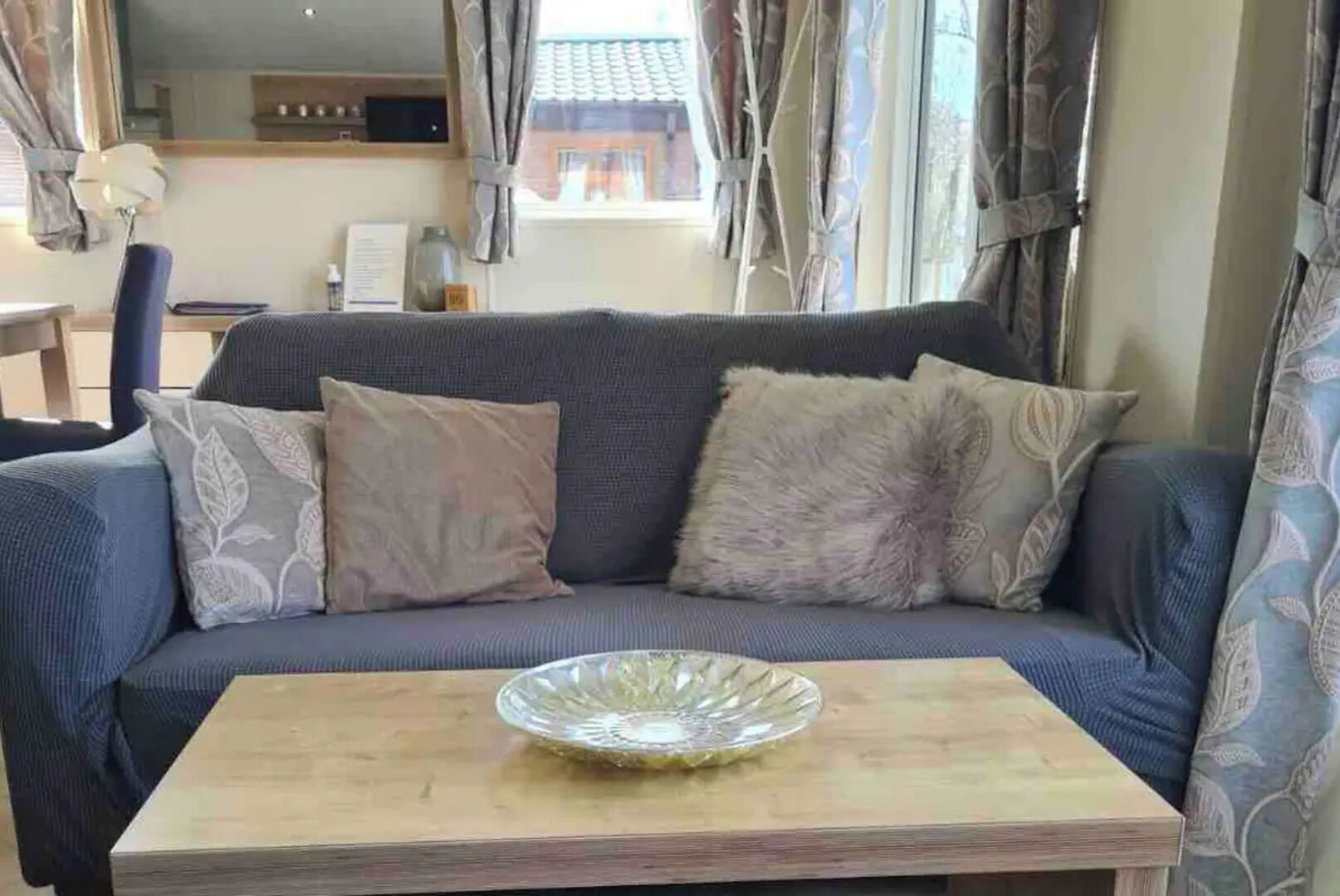 Un salon avec un canapé, une table basse en verre et une vue sur l’extérieur grâce à de grandes fenêtres.