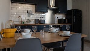 Una cocina moderna con armarios oscuros, un refrigerador negro y una mesa de comedor preparada para cuatro comensales.