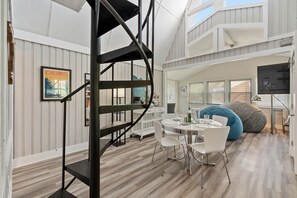 Et moderne interiør med en spiraltrappe, et spiseområde med et rundt bord og stole, og en stor pose-stol.