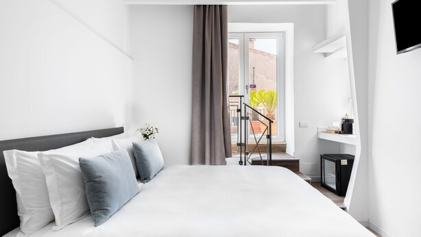 A modern hotel room with a large bed, a small desk with a coffee machine, and a balcony with a view of the city. - Numa Rome Tullo (Rome)