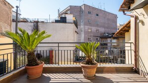 A balcony with two potted plants, a metal railing, and a view of buildings in the background. - Numa Rome Tullo (Rome)