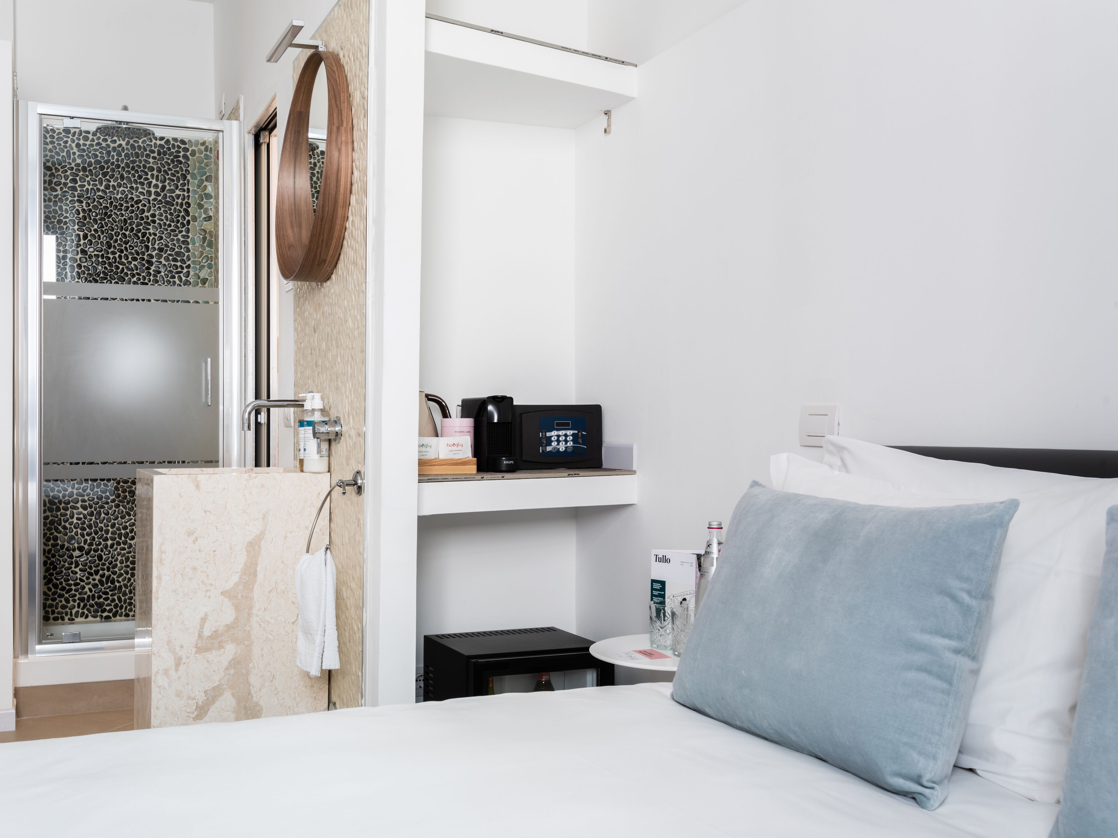 A modern hotel room with a bed, a small bedside table, a microwave, a bottle of water, and a towel hanging on the wall.