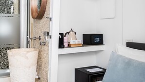 A modern bathroom with a stone mosaic wall, a large round mirror, a sink with a beige marble basin, and a black coffee machine. - Numa Rome Tullo (Rome)