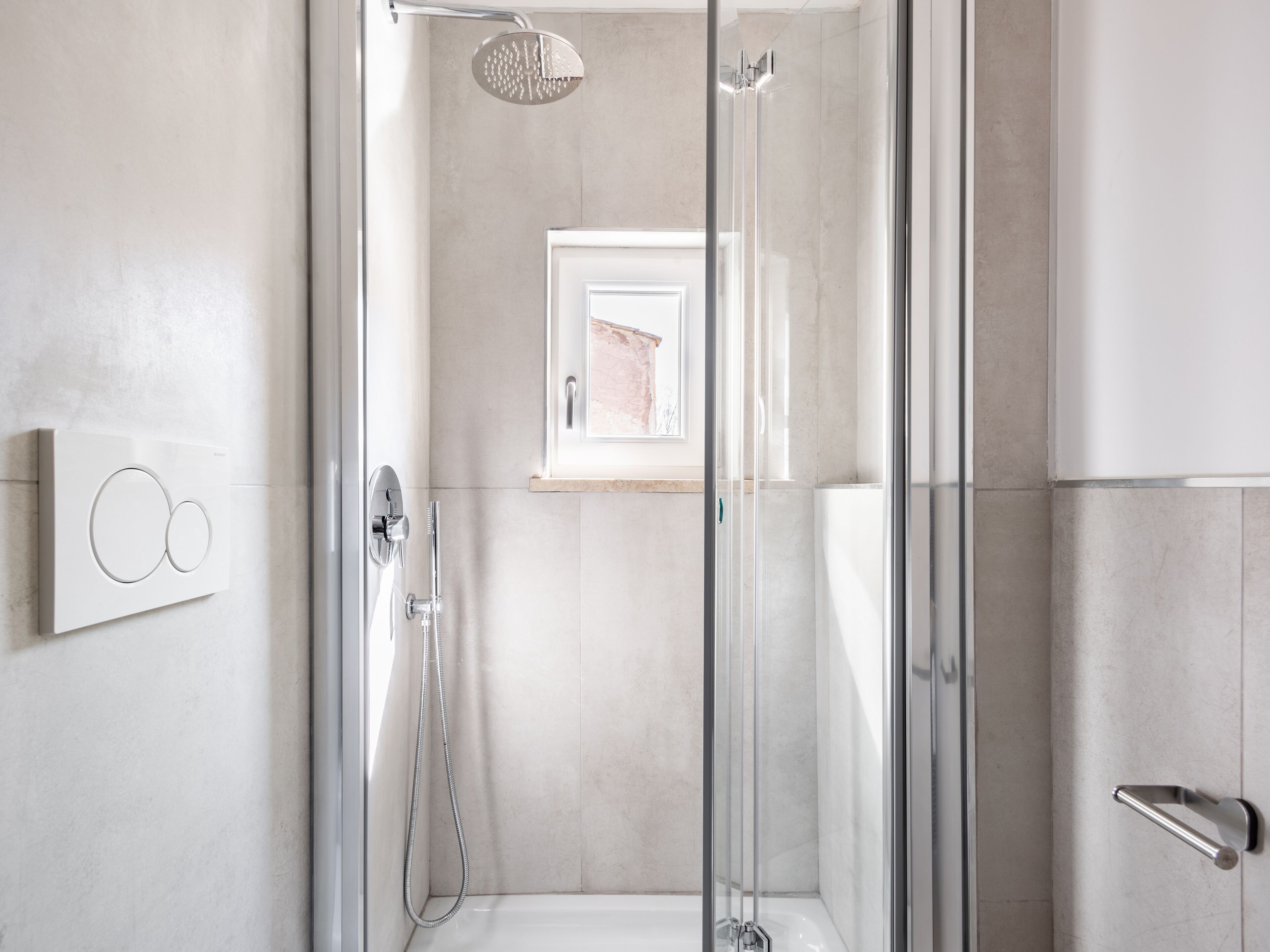 A modern shower area with a glass door, a handheld showerhead, and a wall-mounted control panel.