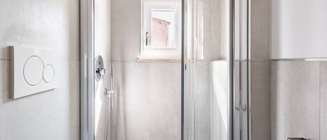 A modern shower area with a glass door, a handheld showerhead, and a wall-mounted control panel.