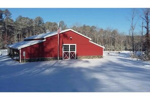A red barn with a white door and a small window, surrounded by snow-covered ground and trees.