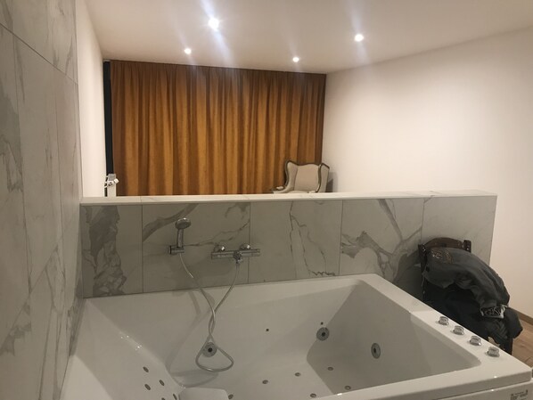 Ein modernes Badezimmer mit einer großen Badewanne, Marmorfliesen und einem Vorhang.